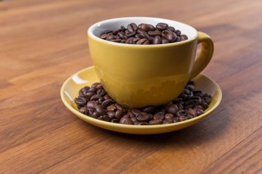 Bir fincan kahve, içinde beyaz olan sarı seramik bir fincana yakın çekim, tahtadan bir yüzey üzerinde kahve çekirdekleri, yatay bir fotoğraf.