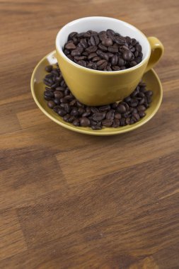 Bir fincan kahve, içinde beyaz olan sarı seramik bir fincana yakın çekim, tahtadan bir yüzey üzerinde kahve çekirdekleri, dikey bir fotoğraf.