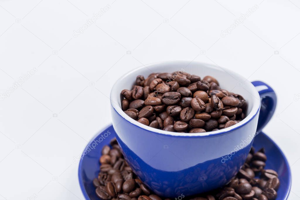 cup of coffee, close-up of a blue ceramic cup with white inside, on a plate with coffee beans on a white surface, horizontal photo