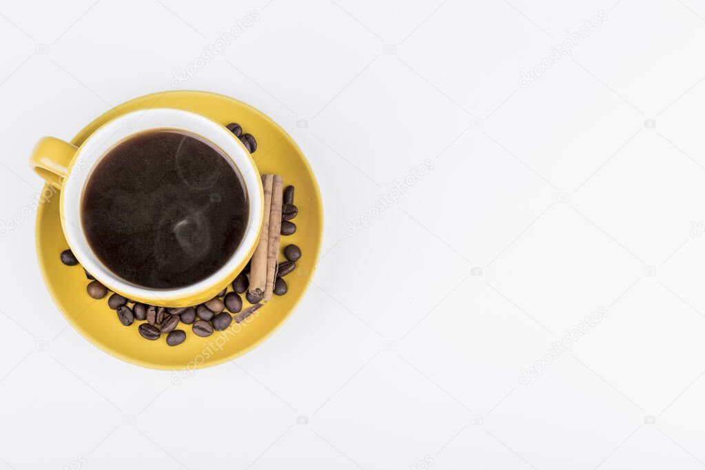 coffee composition, aerial shot of a yellow ceramic mug filled with black coffee, on the coffee plate there are coffee beans and a cinnamon stick, the background surface is white, horizontal photo, there is space for writing