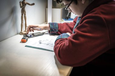 Kırmızı bornozlu bir genç yurttaki odasında Fransızca ödevini yapıyor. Müzik dinliyor ya da akıllı telefonunda podcast yapıyor.