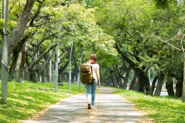Otoyolda yürüyen kepli ve çantalı Latin bir kadın.