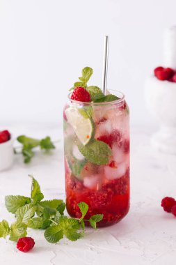 Summer refreshing drinks, fruit and berry raspberry mojito or lemonade with fresh mint, frozen raspberries, slices of lemon, ice, on a light background, dark background
