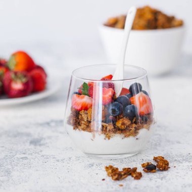 Granola breakfast with fruits, nuts, yogurt in the glass, on a gray stone background, healthy sugar free breakfast, morning meal.