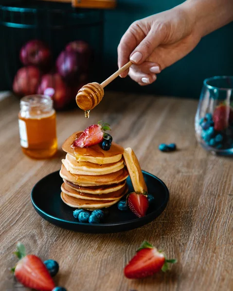 Home-made breakfast or brunch: american style pancakes served with berries and sugar powder on an old cutting board with a cup of black tea