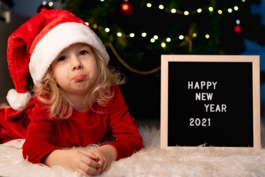 Noel Baba şapkalı güzel bir kız ve kırmızı Noel elbisesi Noel ağacının altında yatıyor.