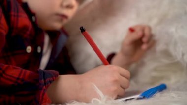 Noel şapkalı küçük bir çocuk Noel ağacının yanındaki kanepede yatan Noel Baba 'ya mektup yazıyor.