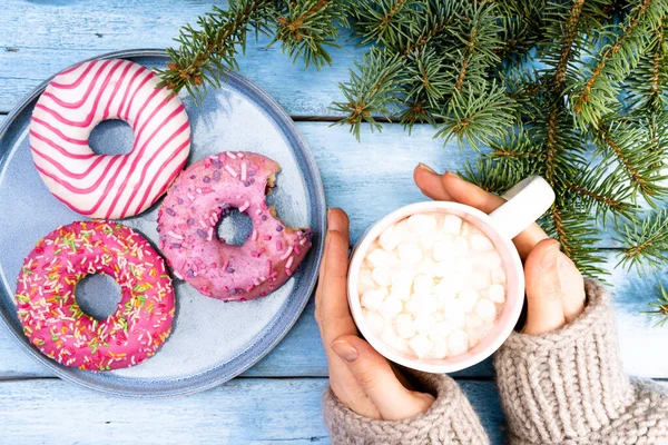 Mavi bir tabakta güzel pembe çörekler ve mavi ahşap bir arka plan, ellerinde lokum olan bir kupa kakao ve Noel ağacının bir dalı. Yüksek kalite fotoğraf