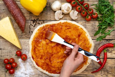 Pizzayı pişirmeden önce ahşap bir masanın üzerinde elle sarılmış hamur sosu ve adım adım tarifi yapmak için gerekli malzemeler.