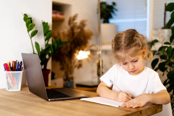 Σοβαρό κορίτσι γελάει με το laptop της και κάνει την εργασία σε ένα σημειωματάριο, σπίτι μάθηση έννοια στην covid 19 πανδημία — Φωτογραφία Αρχείου
