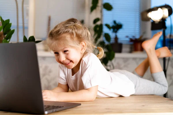 Χαμογελώντας λίγο Καυκάσιος κορίτσι έχει ένα βίντεο κλήση απομακρυσμένη τάξη με έναν δάσκαλο χρησιμοποιώντας ένα φορητό υπολογιστή, χαρούμενος μικρό παιδί χαιρετισμό με έναν δάσκαλο, εκμάθηση σε απευθείας σύνδεση σε έναν υπολογιστή, σπίτι μάθηση έννοια — Φωτογραφία Αρχείου