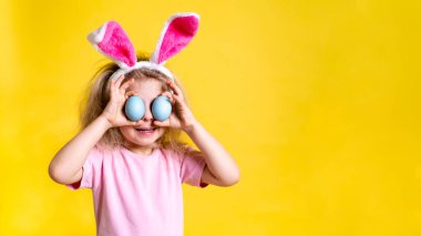 Paskalya tavşanı kulaklı küçük sarışın bir kız ve sarı arka planda paskalya yumurtası, mesaj için yeri var.