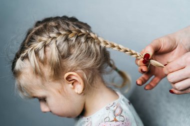 women's hands weave pigtails for a little girl, children's hairstyles at home, a spikelet of hair.