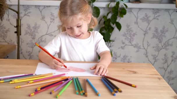 一个小女孩热情地画着一颗心 她独自一人坐在桌旁 手中拿着彩色铅笔 — 图库视频影像