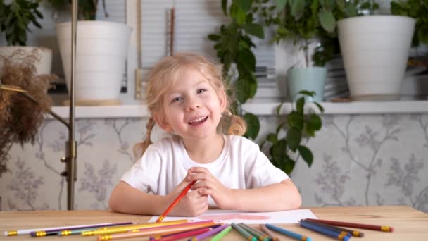 一个有着灰色眼睛和辫子的漂亮的金发小女孩坐在桌旁 微笑着看着摄像机 — 图库视频影像