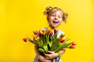 Sarı arka planda, elinde bir buket kırmızı laleyle gülen küçük bir sarışın. tatil kavramı. 