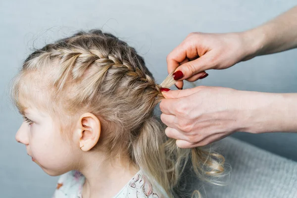 Damskie ręce tkają warkocze dla małej dziewczynki, fryzury dla dzieci w domu, kolce włosów — Zdjęcie stockowe