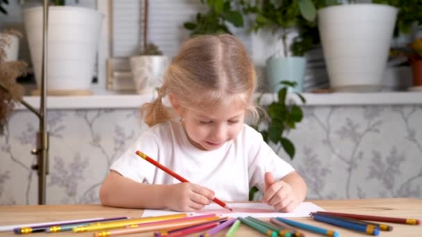 Маленька дівчинка з ентузіазмом малює кольоровими олівцями, сидячи за столом вдома наодинці — стокове відео