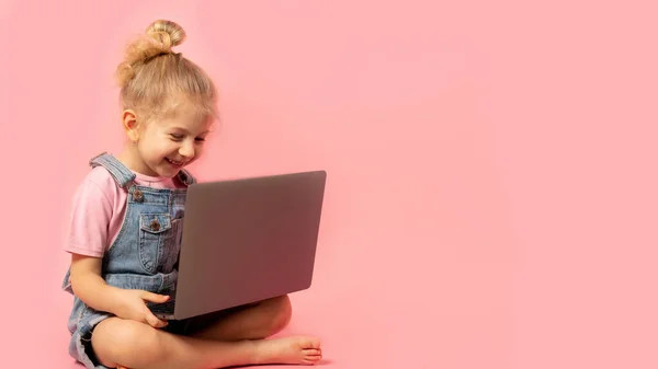 Ένα Χαμογελαστό Κοριτσάκι Κάθεται Ένα Φορητό Υπολογιστή Απομονωμένο Ροζ Φόντο — Φωτογραφία Αρχείου
