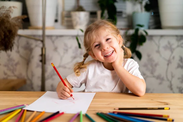 Ένα Μικρό Ξανθό Κορίτσι Κάθεται Στο Τραπέζι Χαμογελώντας Και Ζωγραφίζοντας — Φωτογραφία Αρχείου