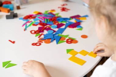 Yuvarlak beyaz bir masada oturan bir kız eğitici oyunlar oynar. Tasarımcı çocukların ellerinden yapılmış bir ev. Anaokullarının gelişim konsepti..