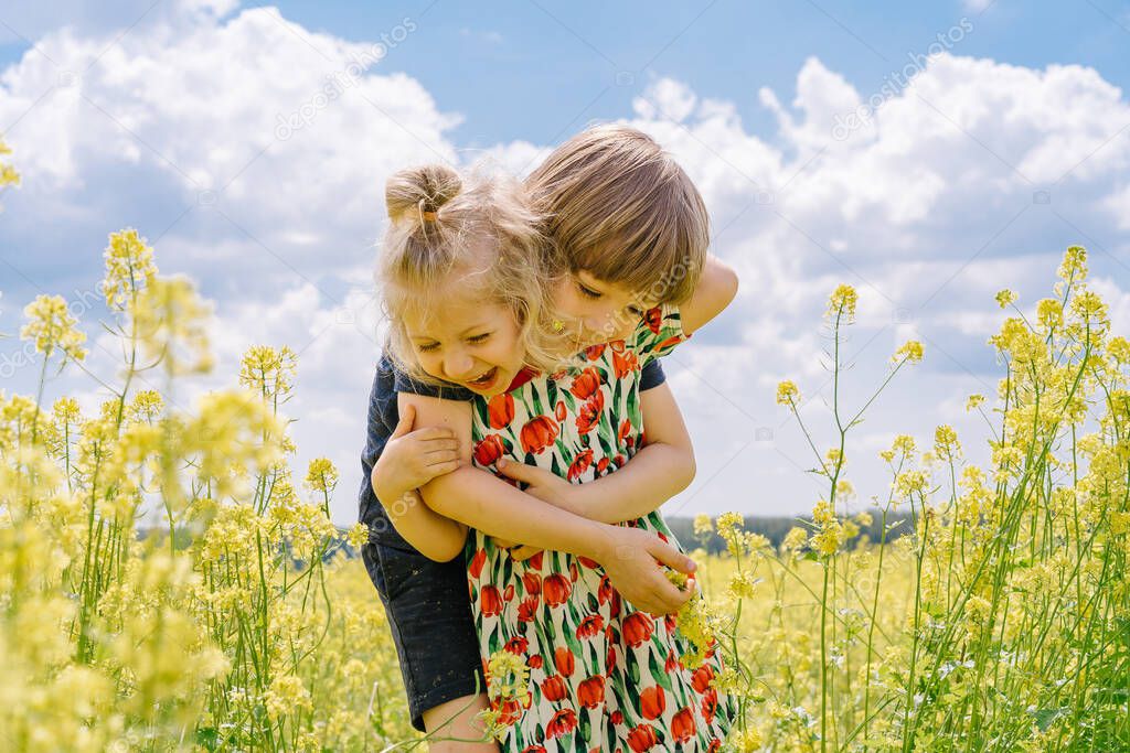 little girl and little boy in rapeseed field, brother and sister in flower field in summer.