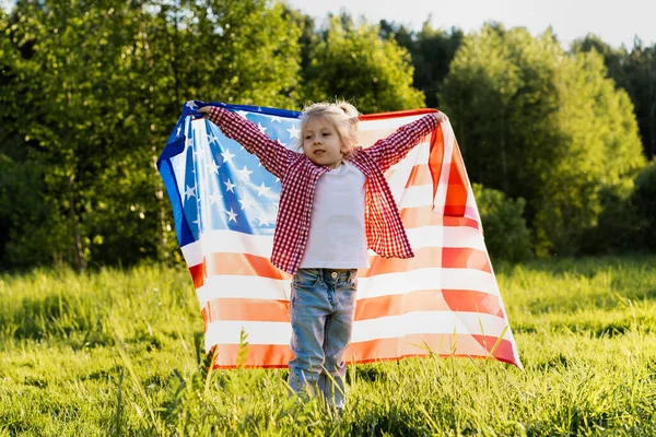 太陽の下で自然の中でアメリカ国旗を持つ美しい小さなブロンドの女の子 — ストック写真
