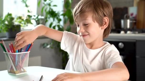 Cute smiling boy draws with colored pencils, at home at the table, happy baby — Vídeos de Stock