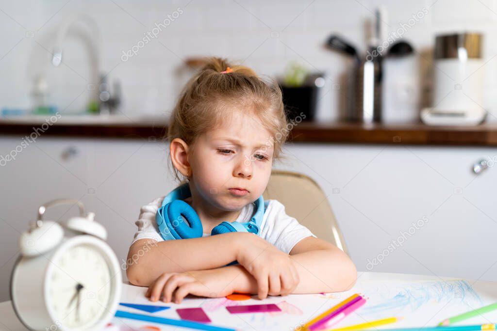 tired little blonde girl at home at the kitchen table, the concept of home education.