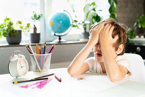 Niño haciendo la tarea en casa en la mesa, el exceso de trabajo de un estudiante de primer grado de estudiar, el estrés de un escolar — Foto de Stock