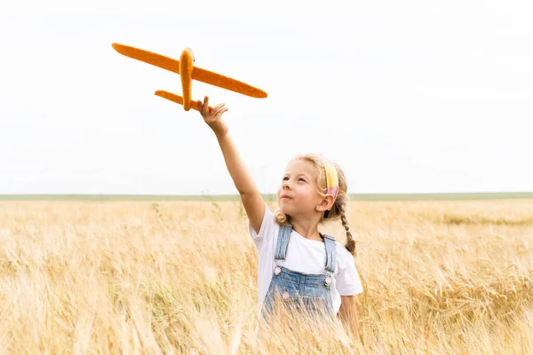 Niña rubia juega avión en el campo de centeno, cosecha de grano — Foto de Stock