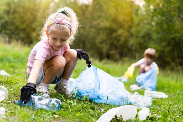 Çocuklar plastik çöpleri çıkarıp açık havada çözünebilir bir çöp torbasına koyuyorlar. Ekoloji, atık işleme ve doğa koruma kavramı. Çevre koruma.