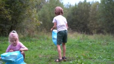 Çocuklar plastik çöpleri çıkarıp açık havada çözünebilir bir çöp torbasına koyuyorlar. Ekoloji, atık işleme ve doğa koruma kavramı. Çevre koruma