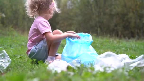 Seorang gadis kecil membuang sampah plastik dan memasukkannya ke dalam kantong sampah biodegradable luar ruangan. Konsep ekologi, pengolahan limbah dan perlindungan alam. Perlindungan lingkungan — Stok Video