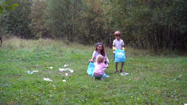 Uma família de voluntários remove o lixo na natureza. mãe e filhos, filha e filho limpar o lixo, garrafas de lixo na floresta, colocá-los em sacos de plástico — Vídeo de Stock