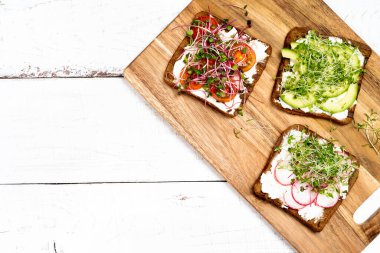 Çeşitli kahvaltı, aperatif kepekli sandviç, krem peynirli tost makineleri, turp, avokado, domates, karides, yumurta, arka planda mikro yeşiller, üst manzara..