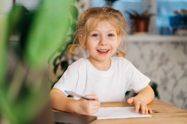 Küçük tatlı sarışın kız yazıyor, evde dizüstü bilgisayarın önünde çalışıyor, internetten öğreniyor, okula geri dönüyor..