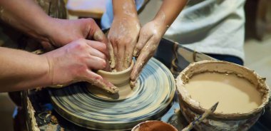 Bir ustayla bir öğrencinin elleri, çömlekçi çarkında bir sürahi yapar. Ellere seçici odaklanma