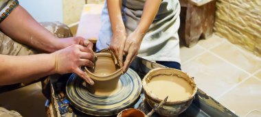 Bir ustayla bir öğrencinin elleri, çömlekçi çarkında bir sürahi yapar. Ellere seçici odaklanma