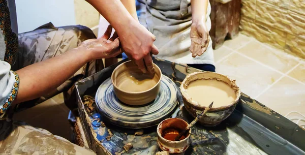 the Hands of a master and a student make a pitcher on a Potters wheel of yellow clay. Selective focus on hands