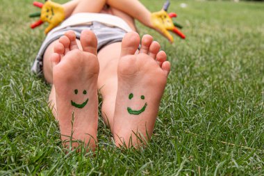 Yeşil çimlerin üzerinde gülümseyen boya desenli çocuk ayakları. Seçici odaklanma. Doğa.