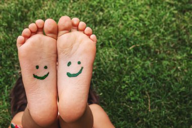 Yeşil çimlerin üzerinde gülümseyen boya desenli çocuk ayakları. Seçici odaklanma. Doğa.
