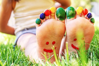 Yeşil çimlerin üzerinde gülümseyen boya desenli çocuk ayakları. Seçici odaklanma. Doğa.