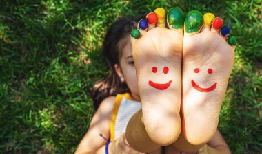 Yeşil çimlerin üzerinde gülümseyen boya desenli çocuk ayakları. Seçici odaklanma. Doğa.