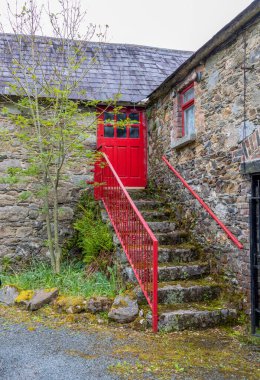 Merdiveni ve kırmızı kapısı olan eski taş bir ev. İrlanda