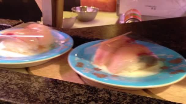 Placas de tren de sushi con el sushi se colocan en una cinta transportadora giratoria — Vídeo de stock