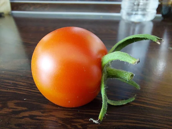 Un tomate rojo cereza maduro yace sobre una mesa marrón. — Foto de Stock
