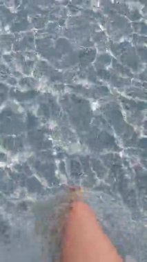 Kadının ayakları saydam deniz suyunda dipte yürüyor.