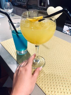 Manikürlü zarif bir kadın eli ferahlatıcı bir kokteyl bardağı tutuyor ve yanında bir bardak daha içki var.