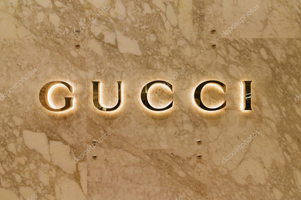 Backlit gold Gucci brand logo on tan marble wall